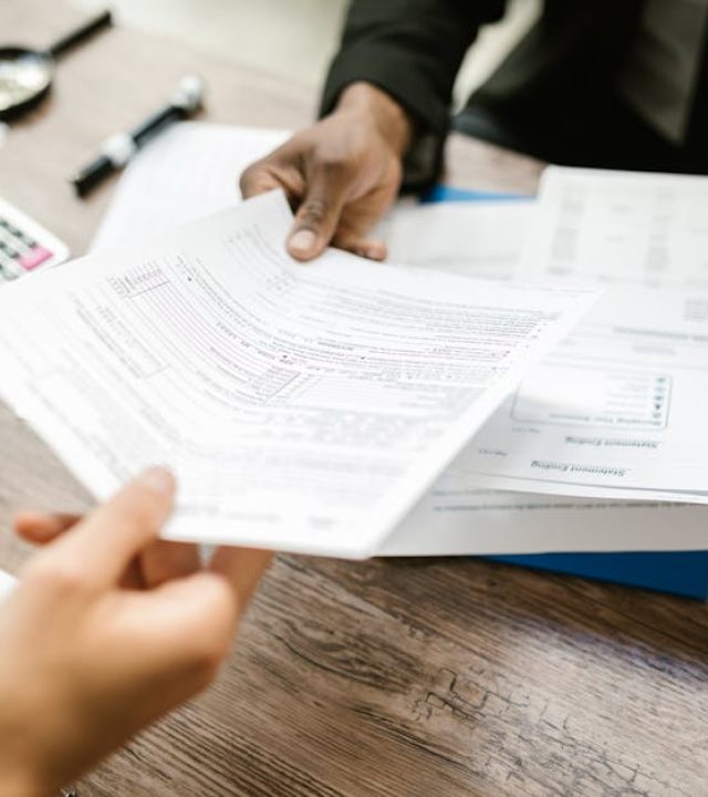 Two professionals exchanging documents in an office setting, focusing on paperwork and data analysis.